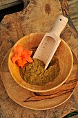 Cumin (Cuminum cyminum) spice powder in a wooden plate and spoon, orange Azalea flower as decoration