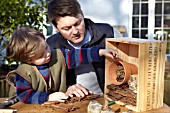INSECT HOUSE BUILDING PROJECT WITH FATHER AND SON.  PLACING MATERIALS IN BOX.  STEP 16