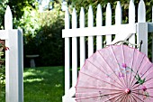 CHINESE SILK PARASOL IN GARDEN WITH WHITE PICKET FENCE AND GATE