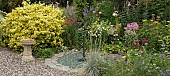 Border of summer flowering herbaceous perennials with sundial set in gravel area