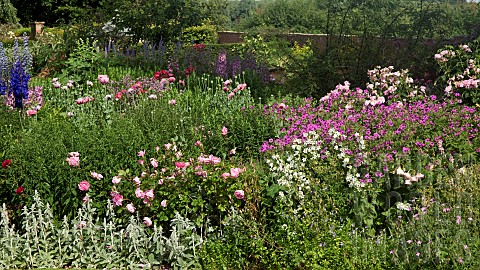Border_of_herbaceous_perennials_brick_walls_surrounded_by_mature_trees__at_Wollerton_Old_Hall_NGS_Ma