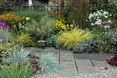 Gravel and paved area with borders of summer flowering herbaceous perennials and ornamental grasses