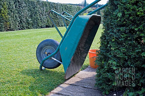 PLASTIC_WHEELBARROW_TIPPED_OVER_AND_RESTING_AGAINST_A_YEW_HEDGE