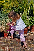 CHILD WATERING PLANT IN POT WITH A WATERING CAN,  SURREY: LATE JUNE